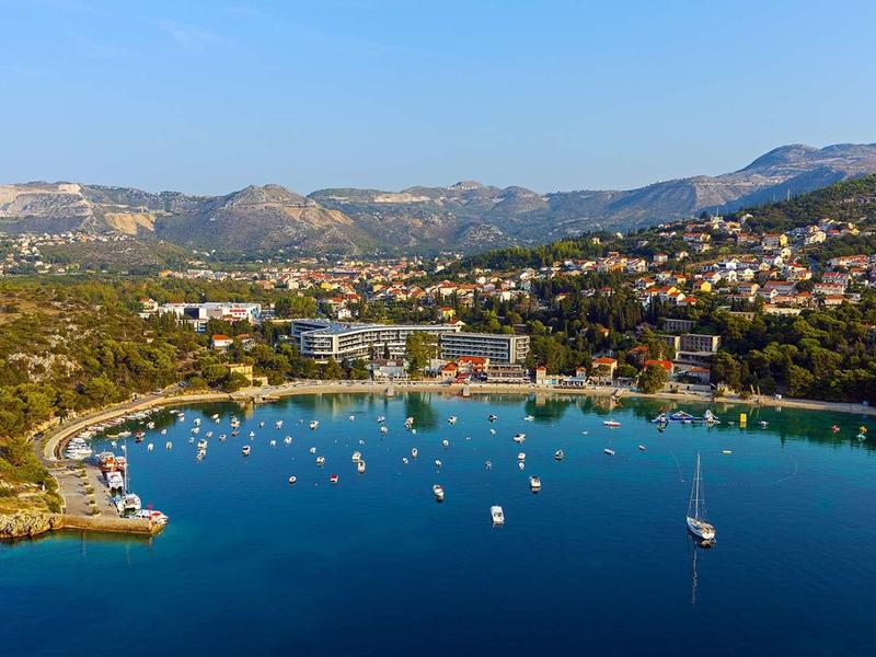 Bucht mit blauem Wasser, zahlreichen Segelbooten und umliegenden grünen Bergen unter klarem Himmel.