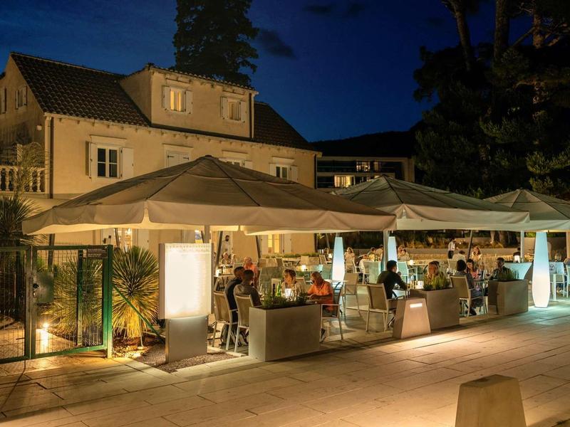 Abendmarkt unter weißen Zelten vor einem beleuchteten Haus mit Verkäufern und Besuchern.