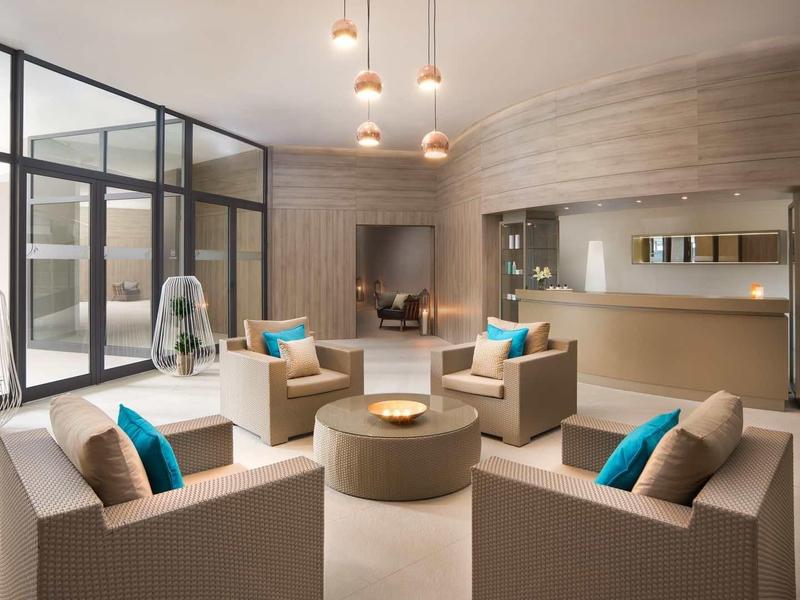 Moderner Wohnzimmerbereich mit hellen Sesseln, blauen Kissen und großen Glasfenstern.