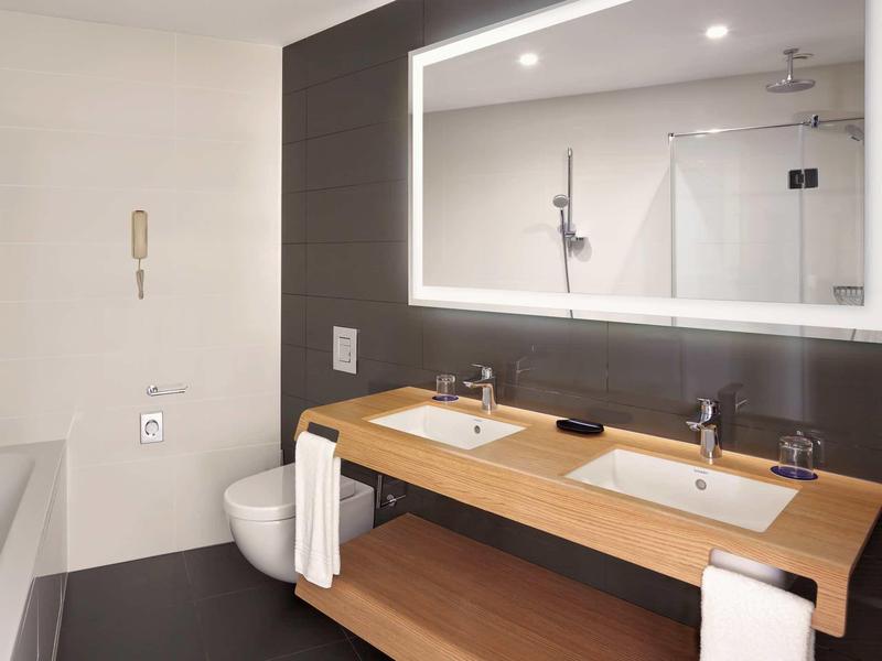 Modernes Badezimmer mit Doppelwaschbecken, beleuchtetem Spiegel und Badewanne links.