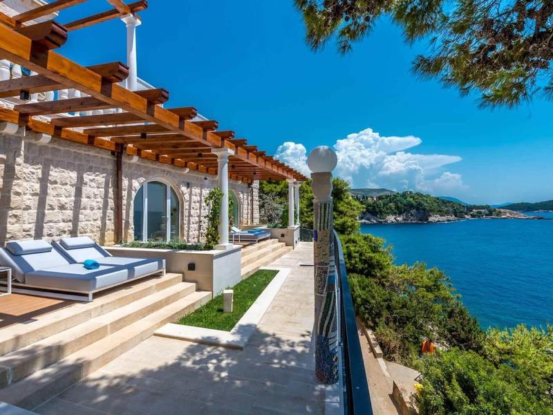 Terrazza di una casa di pietra con lettini e vista sul mare sotto un cielo azzurro.