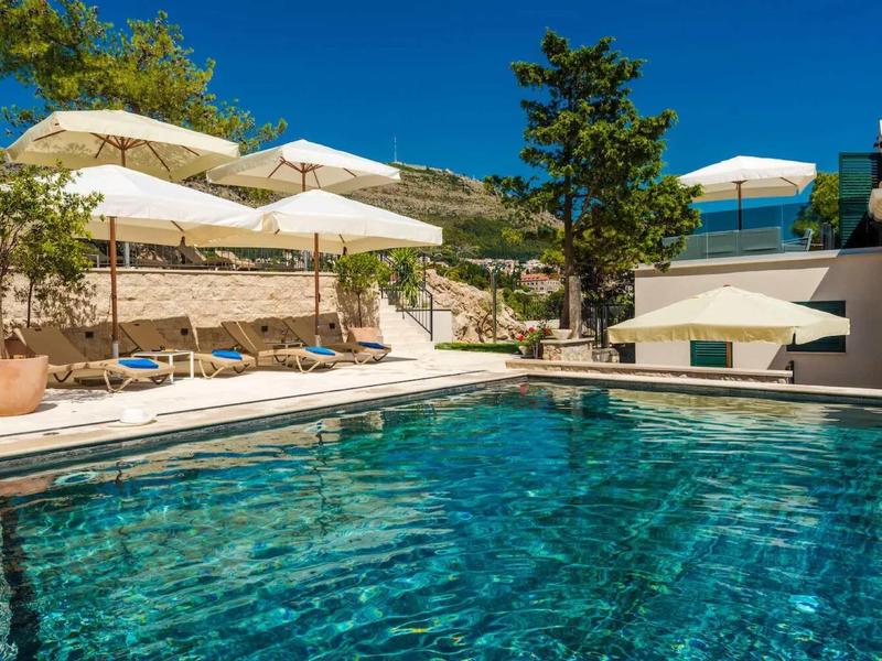 Piscina limpida con ombrelloni bianchi e lettini accanto a un edificio dell'hotel.