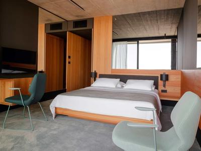 Modern eingerichtetes Hotelzimmer mit großem Bett, Schreibtisch und zwei Stühlen in neutralen Farben.