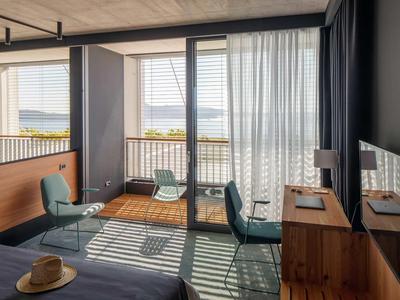 Modernes Hotelzimmer mit Balkon, Meerblick, zwei Stühlen und Schreibtisch.