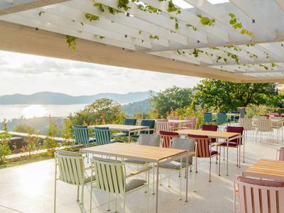 Terrasse mit bunten Metallstühlen und Tischen unter einem weißen, mit Pflanzen bewachsenen Dach.