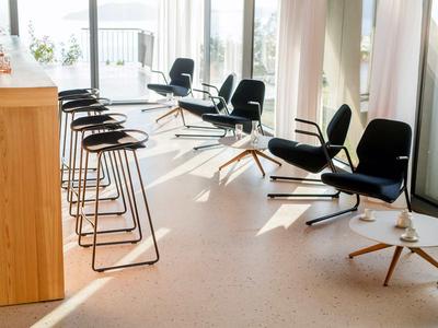 Moderner Wartebereich mit schwarzen Stühlen und Barhockern neben großen Fenstern.