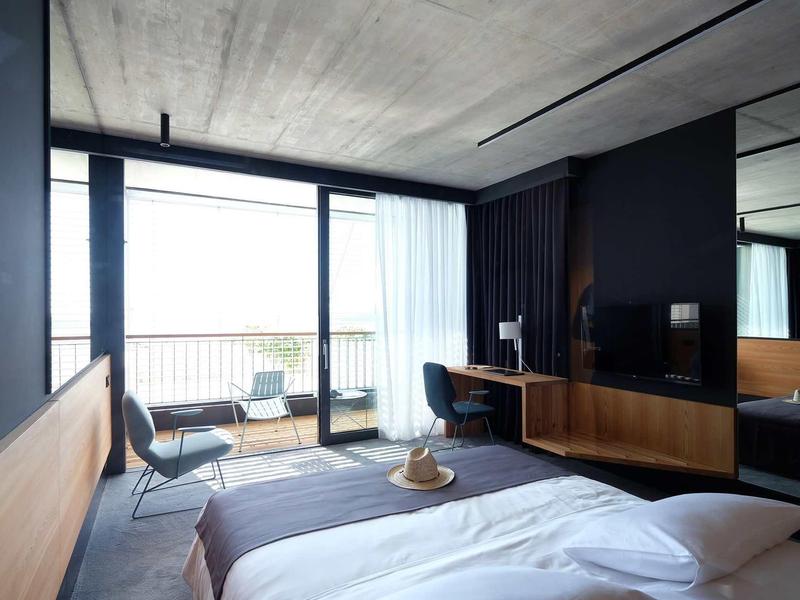 Modernes Schlafzimmer mit großem Fenster, grauen Wänden, Holzmöbeln und minimalistischem Design.