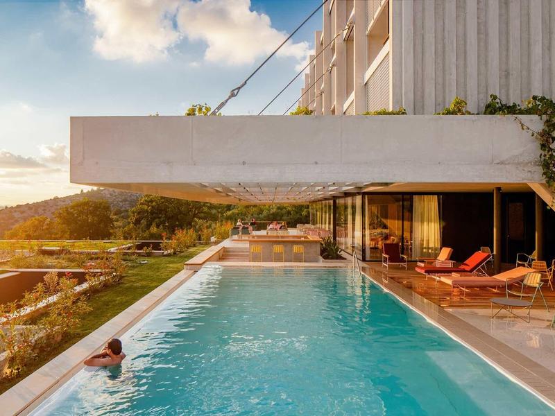 Moderner Pool mit klar blauem Wasser, umgeben von Holzdeck und Sonnenschirmen bei Sonnenuntergang.
