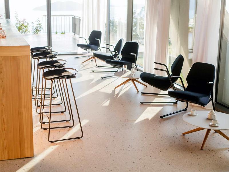 Moderner Sitzbereich mit schwarzen Stühlen und Barhockern, hellem Boden und großen Fenstern.