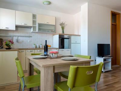 Eetgedeelte met groene stoelen en gedekte tafel naast moderne keuken in lichte kamer.