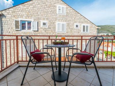 Balkon met twee stoelen en een tafel voor een licht stenen huis onder een blauwe lucht.