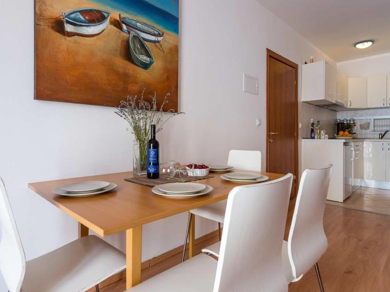 Essbereich mit Holztisch, weißen Stühlen, Geschirr, Vase und moderne weiße Küche im Hintergrund.