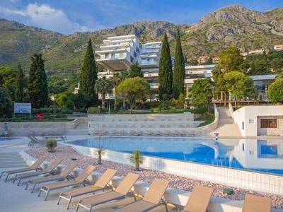Freier Pool mit Liegestühlen, umgeben von Bäumen und Bergen im Hintergrund unter blauem Himmel.