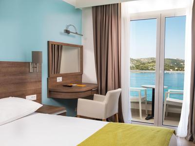 Camera d'hotel luminosa con vista sul mare da un balcone con sedie.