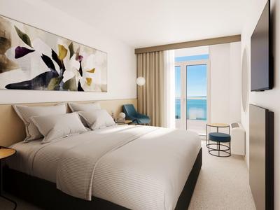 Camera d'hotel moderna con letto matrimoniale, opera d'arte sulla parete e balcone con vista mare.