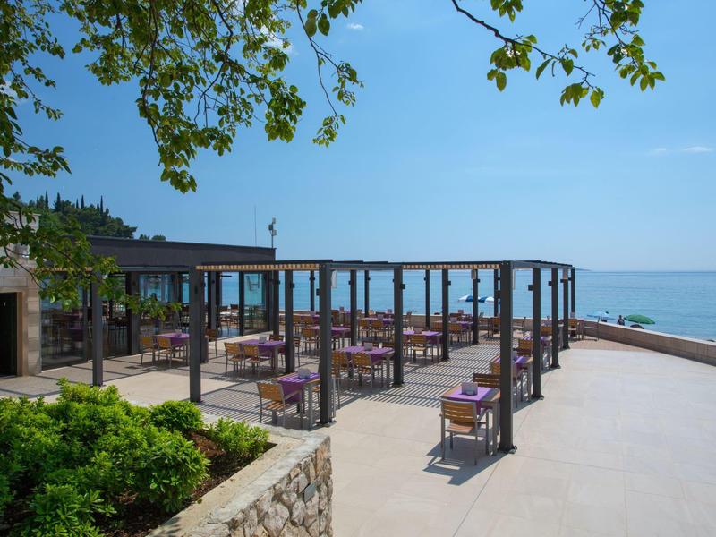 Terrazza con tavoli e sedie con vista sul mare sotto un cielo limpido.