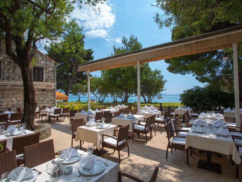 Ristorante all'aperto con tavoli apparecchiati con vista su alberi e acqua.