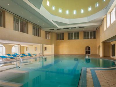 Piscine intérieure avec eau bleue, transats et éclairage chaleureux dans un hôtel.