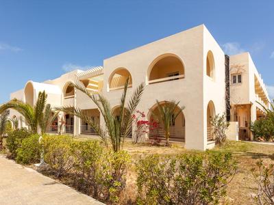 Moderner, hell gestrichener Gebäudekomplex mit Bögen und Palmen vor blauem Himmel.