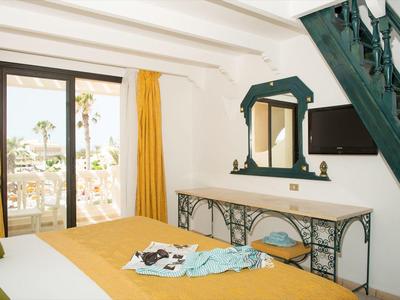 Chambre lumineuse décorée avec housse de lit jaune et accès à un balcon avec vue sur la mer.