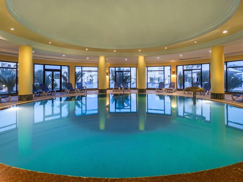 Piscine intérieure ronde dans un hôtel moderne avec de grandes fenêtres et des chaises longues confortables