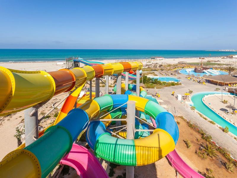 Des toboggans colorés mènent à une piscine dans un parc aquatique près de la plage.