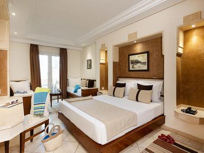 Helles Hotelzimmer mit Doppelbett, Sitzecke, Schreibtisch und großem Fenster mit Blick auf die Stadt.