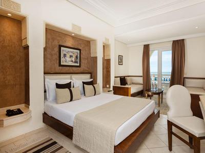 Helles Hotelzimmer mit Doppelbett, Sitzbereich und großem Fenster mit Blick aufs Meer.