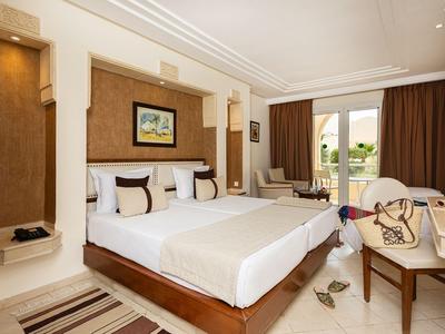 Helles Hotelzimmer mit großem Bett, Kunstwerk an der Wand und Blick auf den Balkon.