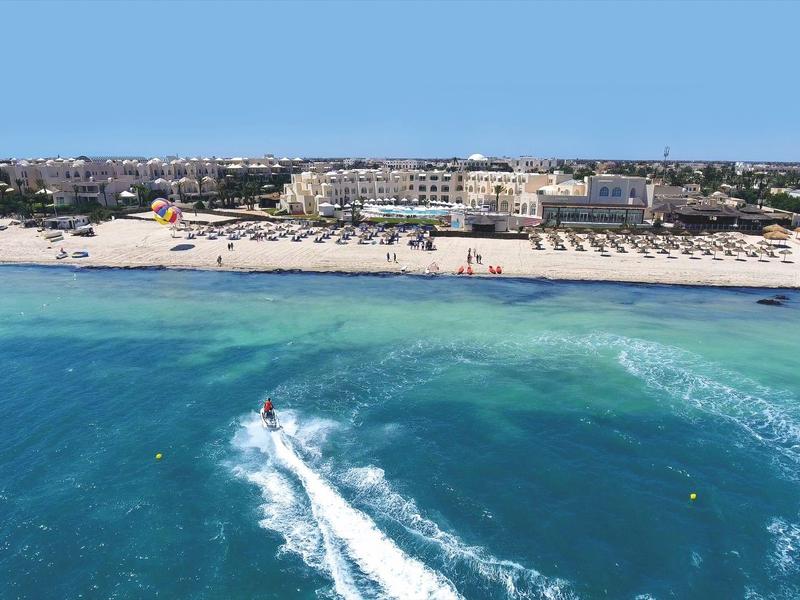 Luchtfoto van een strandresort met helderblauw water en iemand die dichtbij de kust jetskiÃ«t.