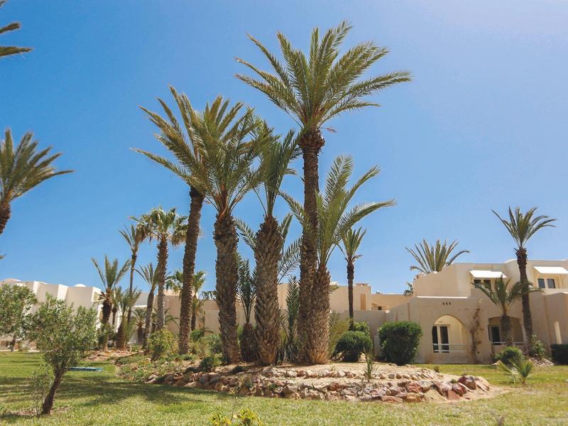 Zonnig resort met palmbomen en beige gebouwen onder een heldere blauwe lucht.