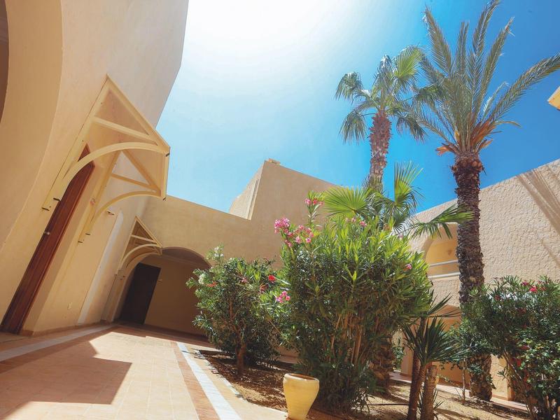 Zonnige binnenplaats met palmbomen en bogen bij een hotel.