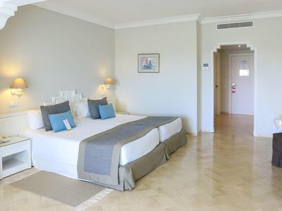 Helles Hotelzimmer mit zwei Einzelbetten, weißen Möbeln und beigem Marmorboden.