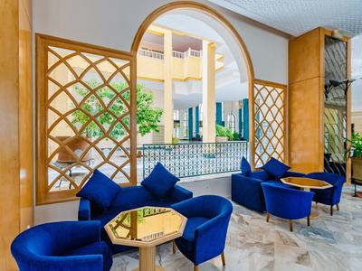 Moderner Wartebereich mit blauen Sesseln, Holzwänden, Glasbistrotischen und Pflanzen in hellem Raum.