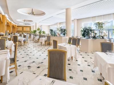 Helles, elegantes Restaurant mit gedeckten Tischen, grauen Stühlen und großen Fenstern.