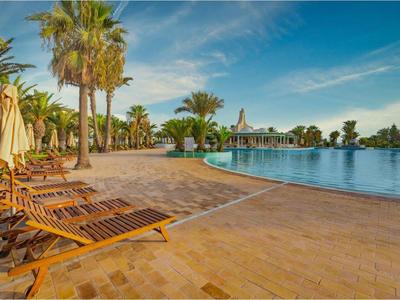 Liegestühle und Sonnenschirme an einem Pool mit Palmen unter blauem Himmel.