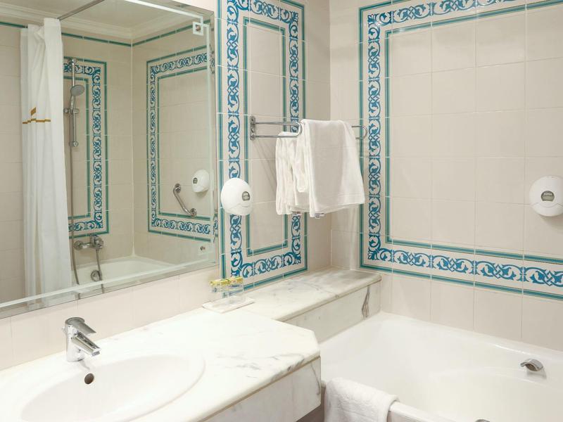 Helles Badezimmer mit weißer Badewanne, Waschbecken, großem Spiegel und blauen Fliesenakzenten.