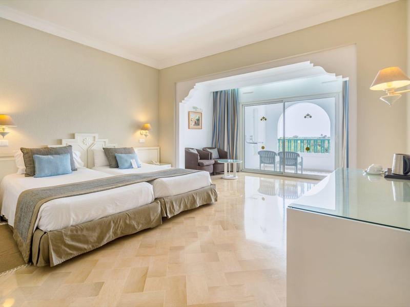 Helles Hotelzimmer mit zwei Einzelbetten, großen Fenstern und modernem, schlichtem Design.