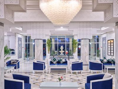 Elegante salón de hotel en blanco y azul con suelo de mármol y candelabro.