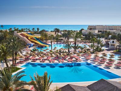 Großer Hotelpool mit Wasserrutschen, Palmen und vielen Liegen unter blauem Himmel.