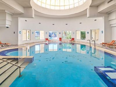 Gran piscina cubierta circular con claraboya y tumbonas a los lados.