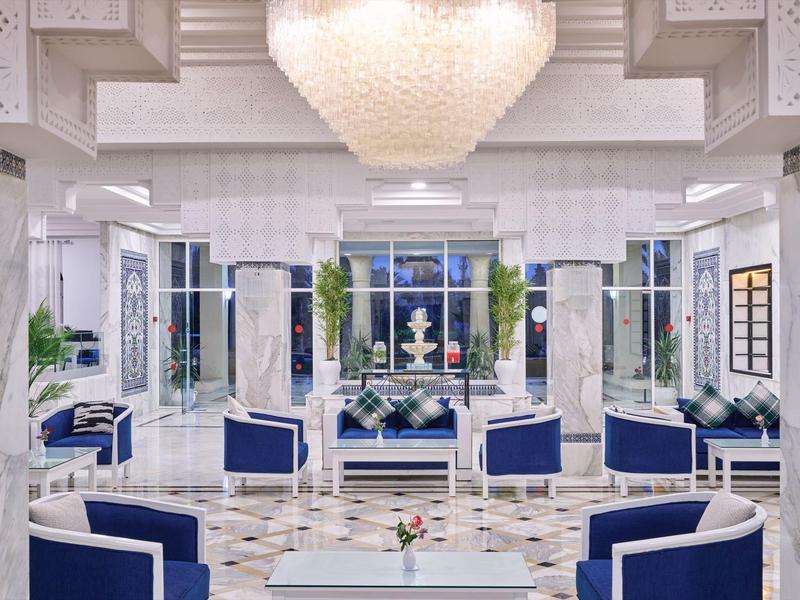Elegante salón de hotel en blanco y azul con suelo de mármol y candelabro.