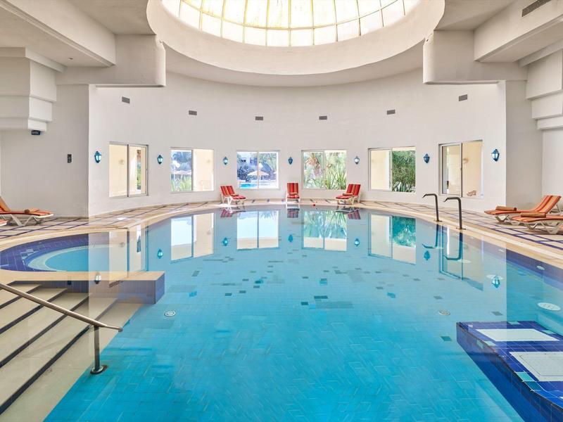 Gran piscina cubierta circular con claraboya y tumbonas a los lados.