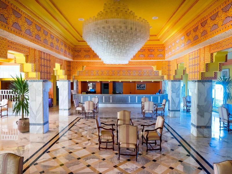 Amplio y lujoso lobby de hotel con suelo de mármol, sillas elegantes y gran araña