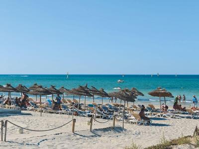 Strand mit vielen Liegestühlen und Strohhutsonnenschirmen vor blauem Meer und klarem Himmel