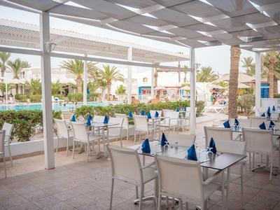 Freiluftrestaurant mit dekorierten Tischen und Blick auf Palmen und Hotelgebäude.