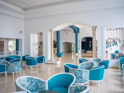 Área de salón elegante y luminosa en hotel con sillones azules y suelo de mármol crema.
