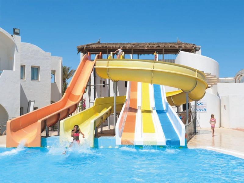 Toboganes de agua coloridos en una piscina frente a un edificio blanco bajo un cielo azul claro