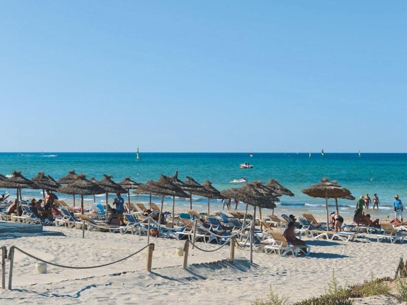 Playa con sombrillas y tumbonas junto al mar azul claro bajo cielo despejado.
