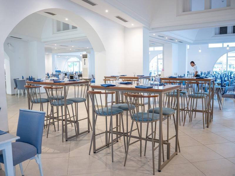 Espacio luminoso de hotel con mesas altas modernas y sillas sobre suelo de baldosas claras.